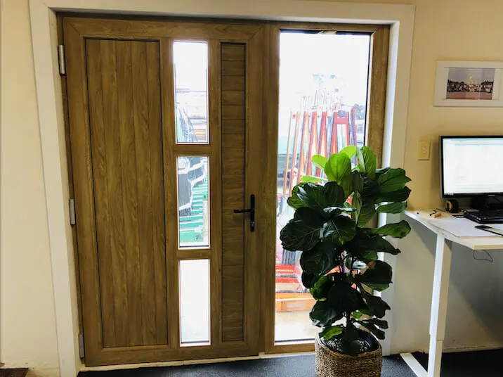 Doors A wooden door with large glass panels, next to a potted plant and a computer desk.