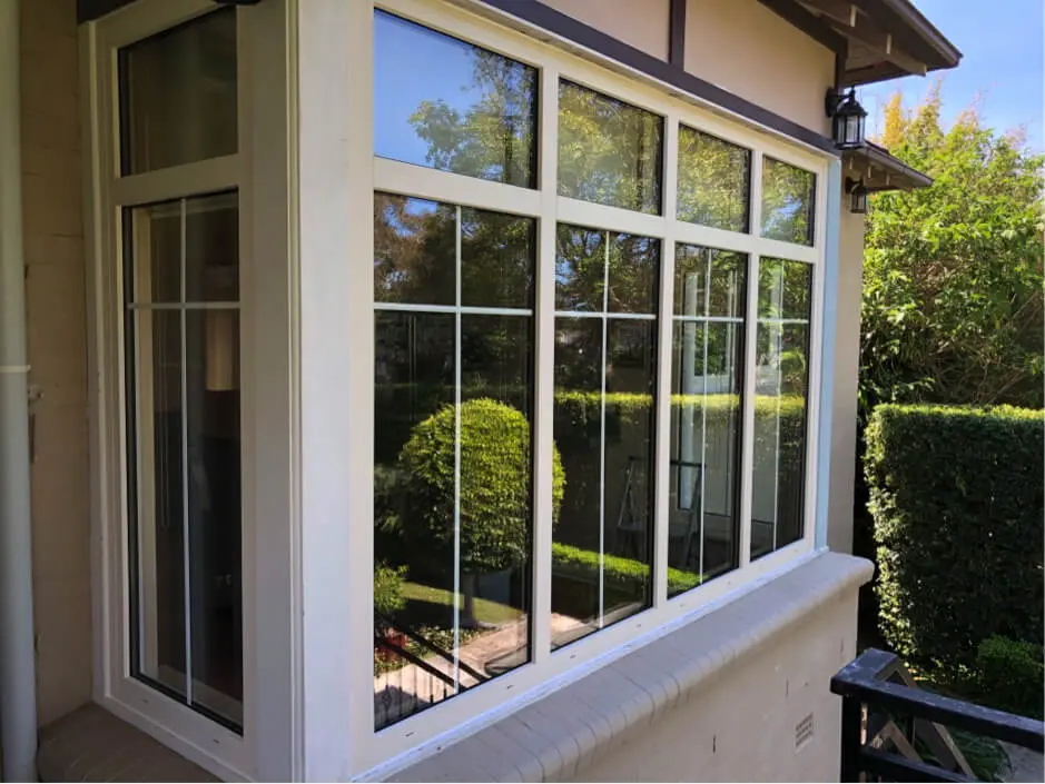 Windows-Options A large window with multiple panes showing greenery outside, a well-trimmed hedge, and a clear blue sky.