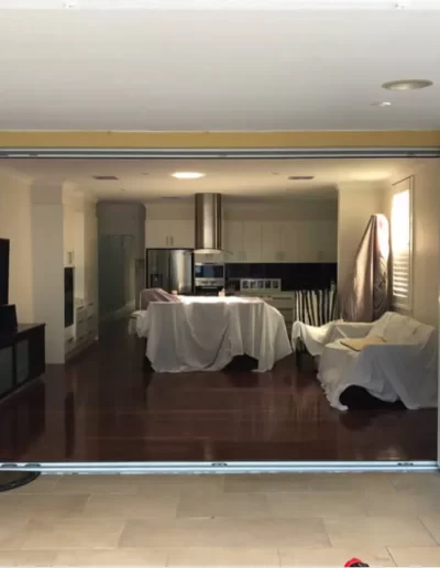 A wide open folding door leading to a modern kitchen with covered furniture.