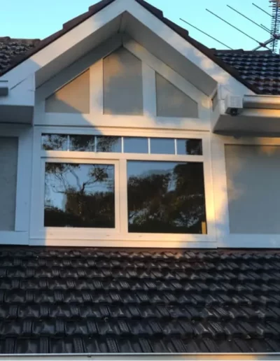 A modern house exterior featuring a sloped roof, a large window, and an antenna.