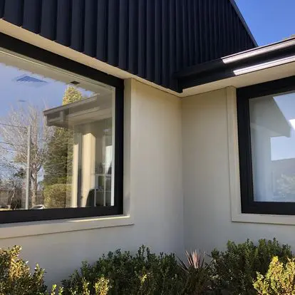 Close-up of a modern house corner with large windows and a black roof.